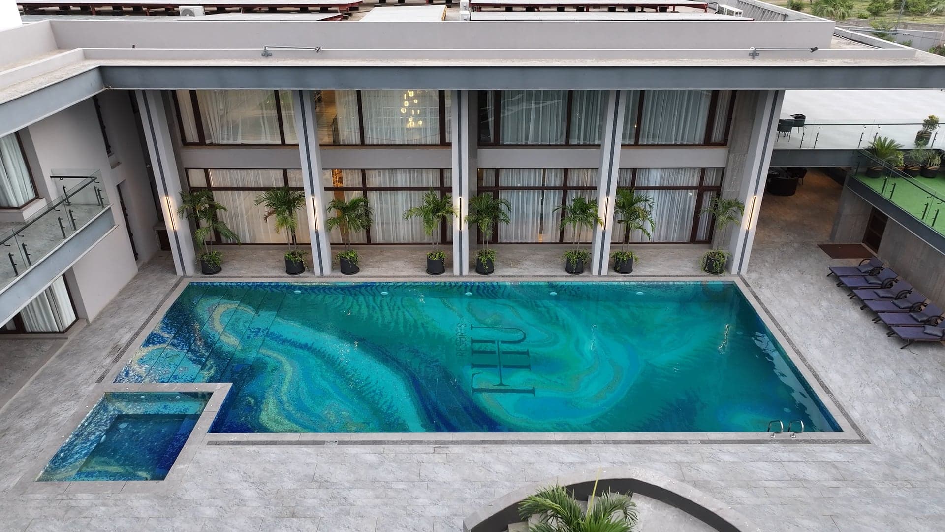 Olympic-style main swimming pool at FHU Resorts Karachi with a mosaic FHU crest, poolside recliner chairs and changing rooms