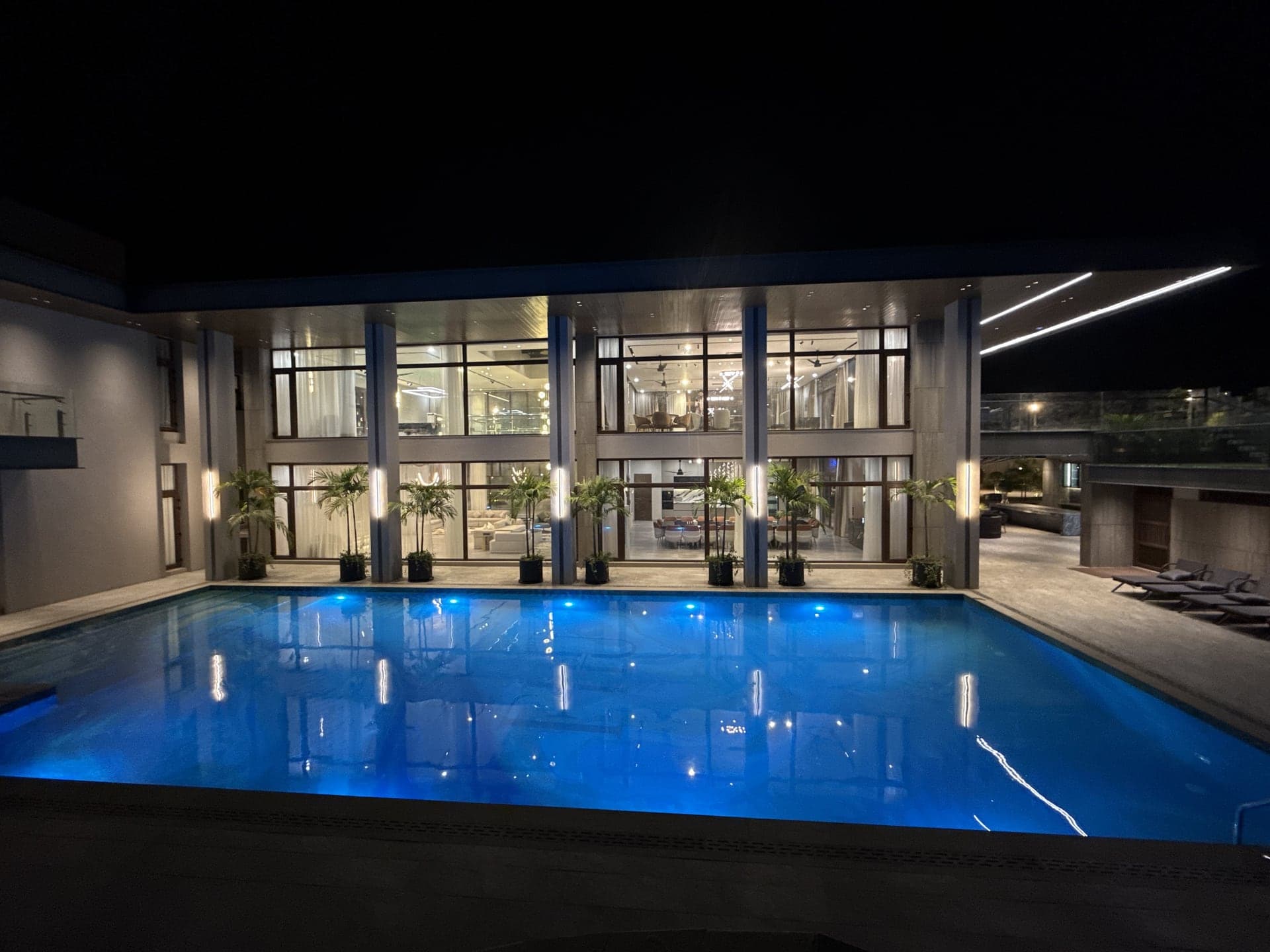 The main swimming pool lit blue at night with the villa's glass facade glowing behind at FHU Resorts Karachi